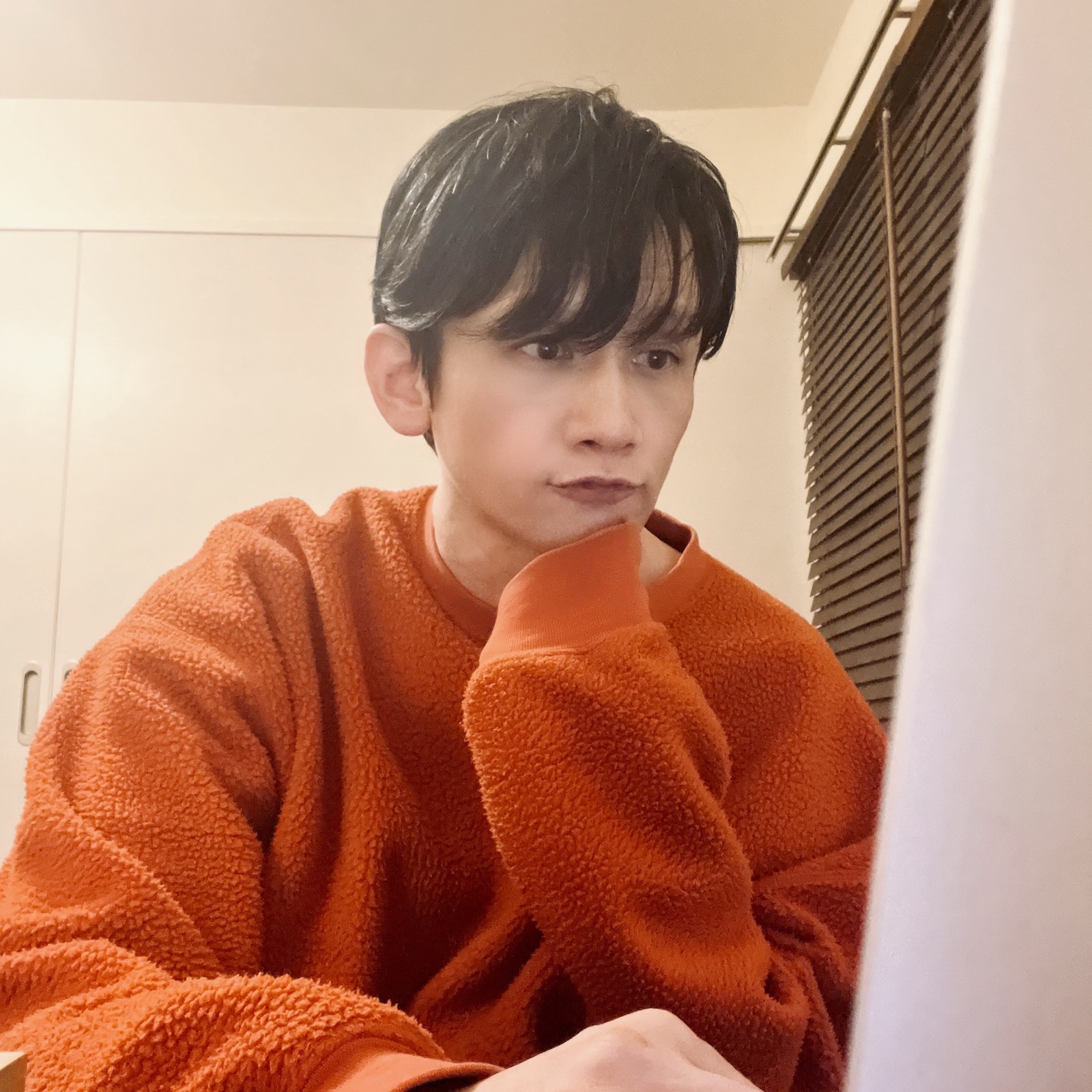 ムーンテッド(MoonTed)の日記より、頬杖をついて画面を見つめるムーンテッド(MoonTed)のセラピストAKI。オレンジのセーター姿