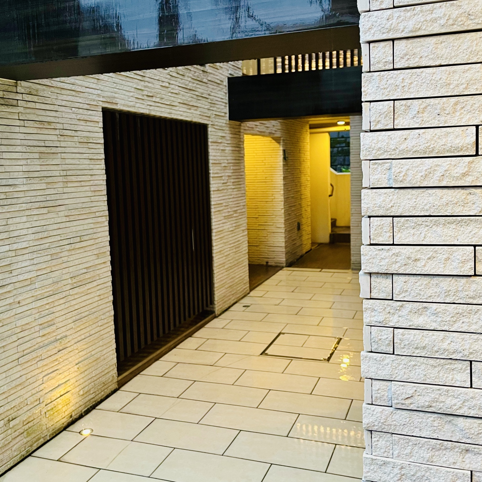 ムーンテッド(MoonTed)の日記より、雨に濡れたマンションの通路。石張りの壁と、足元に灯るライト