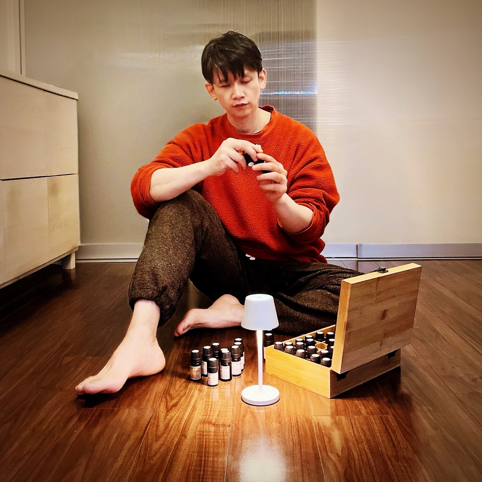 MoonTed Diary: Therapist AKI sitting barefoot on the floor with a small essential oil bottle, oils in a wooden box and a white lamp in front