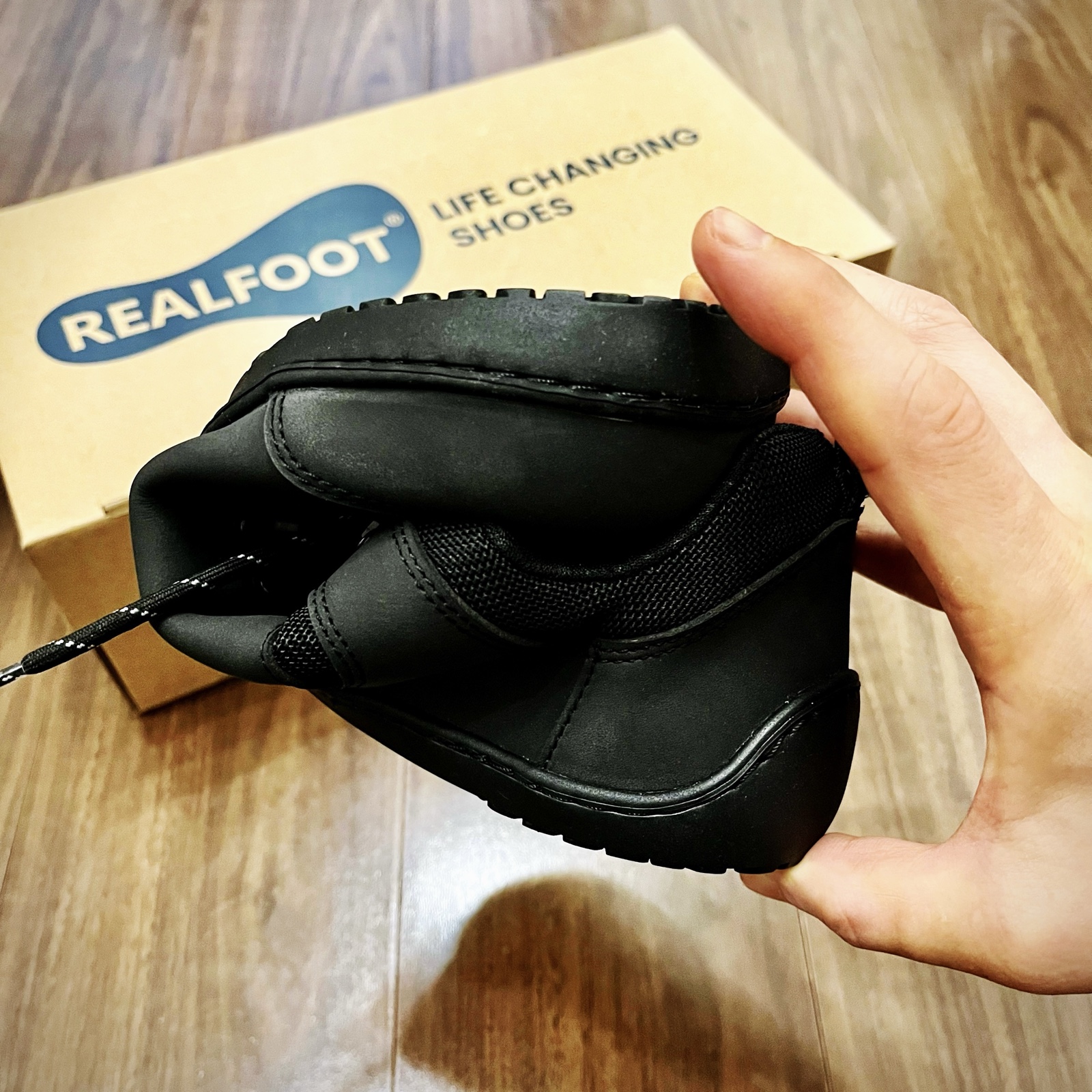 ムーンテッド(MoonTed)の日記より、手で曲げたRealfootの黒いベアフットシューズ。奥に「LIFE CHANGING SHOES」と書かれた箱