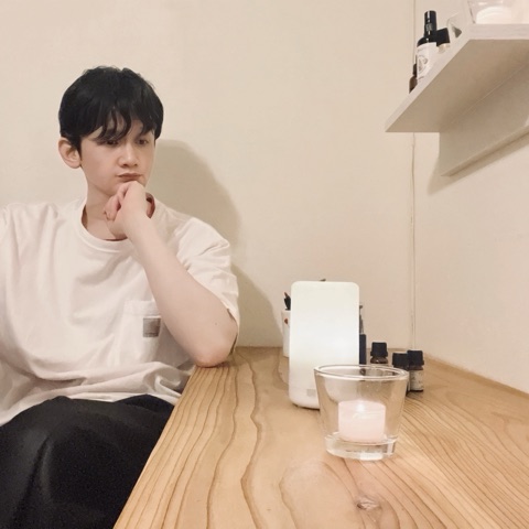 ムーンテッド（MoonTed）の日記より、机に頬杖をついて考え込むムーンテッド（MoonTed）のセラピストAKI。手前にキャンドル、棚に遮光瓶