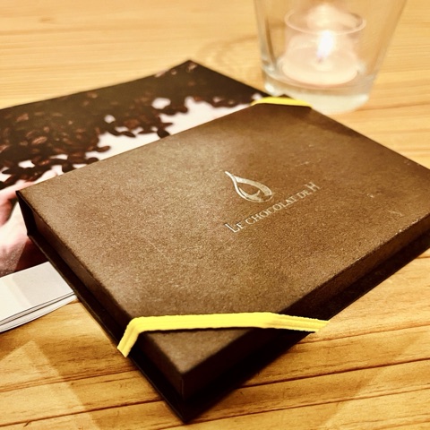 ムーンテッド（MoonTed）の日記より、ル ショコラ ドゥ アッシュの焦げ茶色の箱に、黄色のゴムバンド。奥にキャンドル