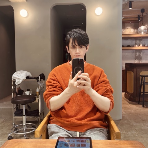 ムーンテッド（MoonTed）の日記より、ヘアサロン「ere」の鏡の前でスマートフォンを構えるムーンテッド（MoonTed）のセラピストAKI。オレンジのセーター姿