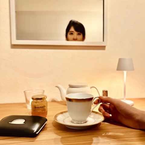 ムーンテッド（MoonTed）の日記より、鏡に映る女性の顔と、ティーカップに添えた手。テーブルにポットとはちみつの瓶、白いランプ