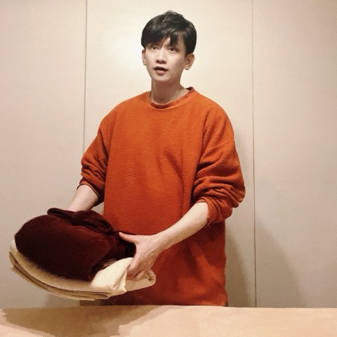 ムーンテッド（MoonTed）の日記より、たたんだ赤いブランケットとタオルを抱え、施術台の向こうに立つムーンテッド（MoonTed）のセラピストAKI