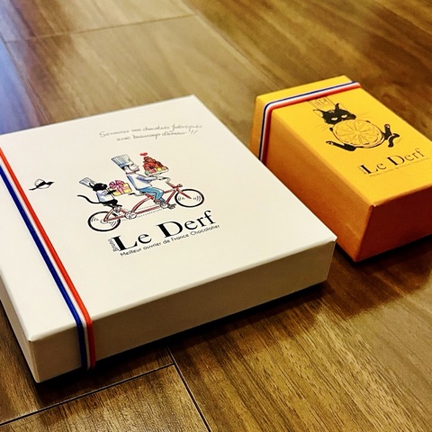 ムーンテッド（MoonTed）の日記より、ル・デルフ（Le Derf）のチョコレートの箱2つ。自転車に乗るシェフのイラストの白い箱と、猫のイラストの黄色い箱