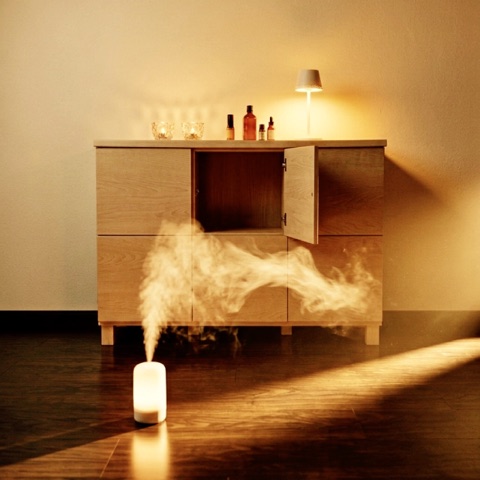MoonTed Diary: White mist rising from an aroma diffuser on the floor, with a wooden chest, amber bottles, candles and a lamp in warm light