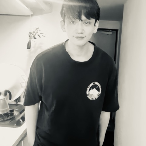 ムーンテッド（MoonTed）の日記より、サロンのキッチンに立ち、少し微笑むムーンテッド（MoonTed）のセラピストAKI。黒いTシャツ姿のモノクロ写真