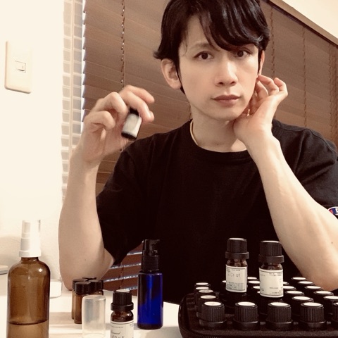 ムーンテッド（MoonTed）の日記より、精油の小瓶を手に、頬に手をあてるムーンテッド（MoonTed）のセラピストAKI。手前に並ぶたくさんの精油