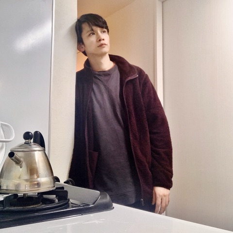 ムーンテッド（MoonTed）の日記より、キッチンの壁にもたれるムーンテッド（MoonTed）のセラピストAKI。えんじ色のフリースジャケット姿、手前にケトル