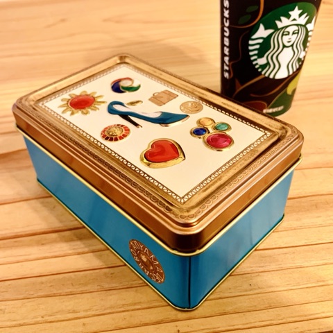 ムーンテッド（MoonTed）の日記より、青山デカーボの缶。蓋に宝石やハイヒールのモチーフ、奥にスターバックスのカップ
