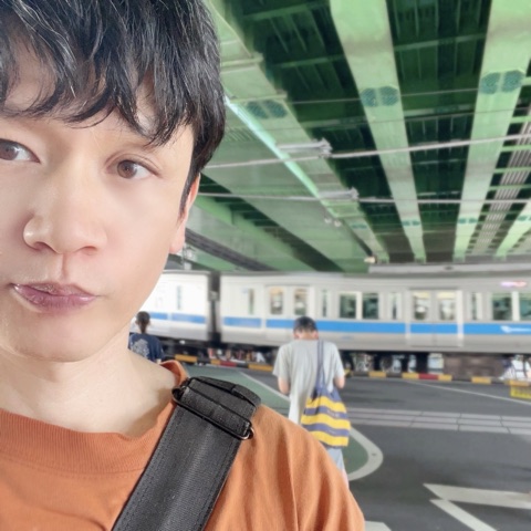 ムーンテッド（MoonTed）の日記より、代々木八幡の踏切で自撮りするムーンテッド（MoonTed）のセラピストAKI。後ろを小田急線の電車が通過する